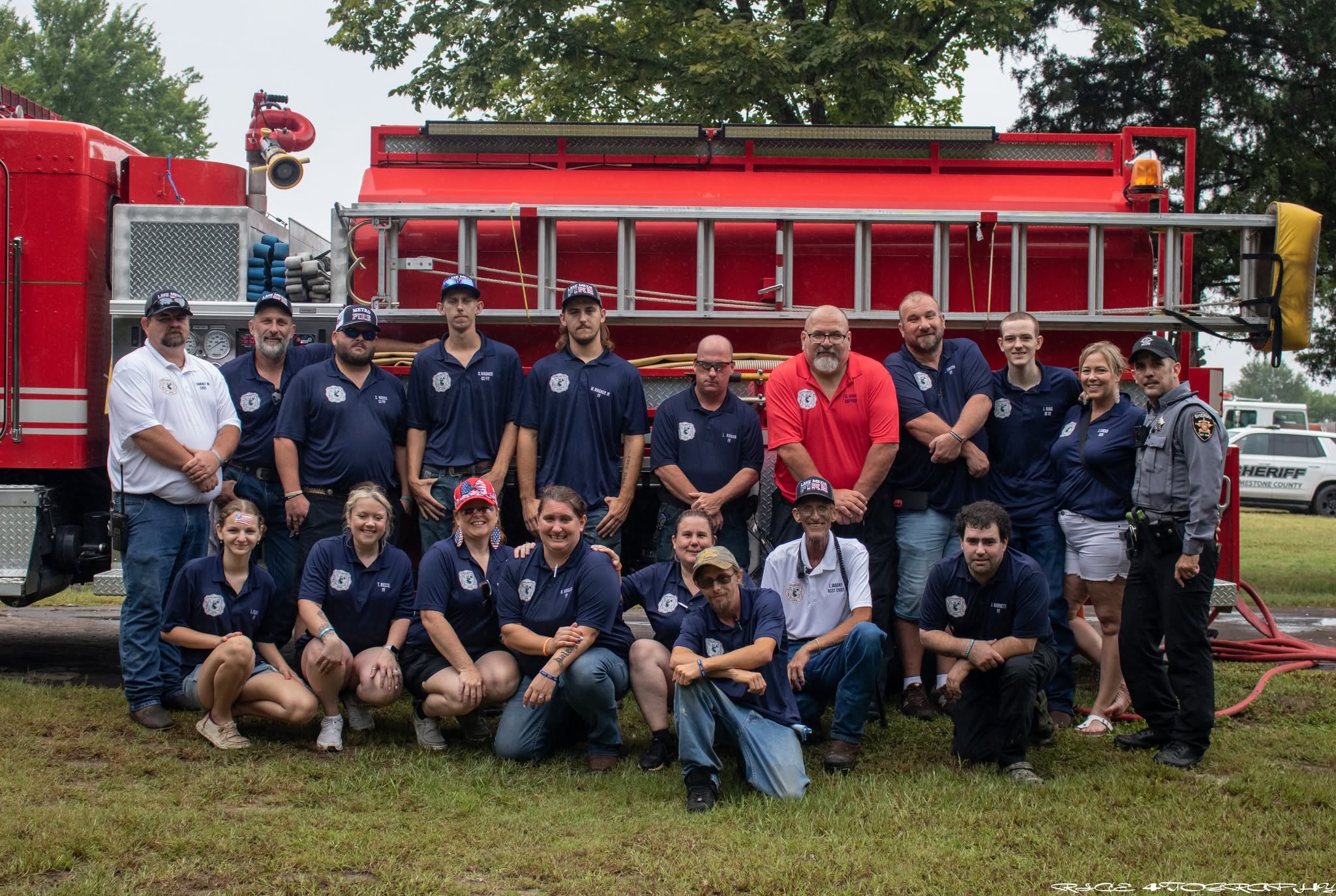 Group of 18 people posed in two rows in front of a red Lake Mexia fire truck.